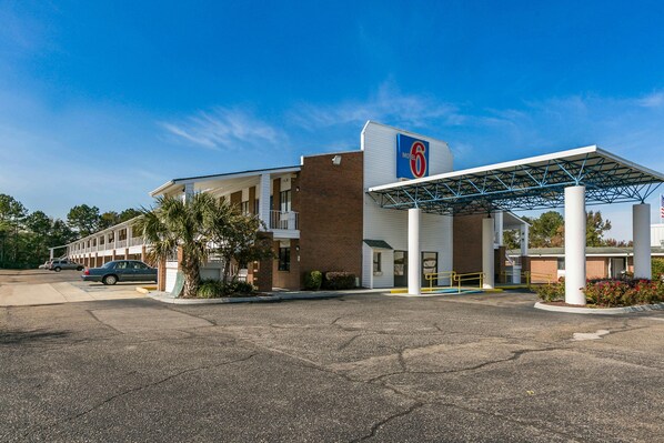 Un motel con área de estacionamiento techada, un edificio de ladrillo y un letrero que indica que es un Motel 6.