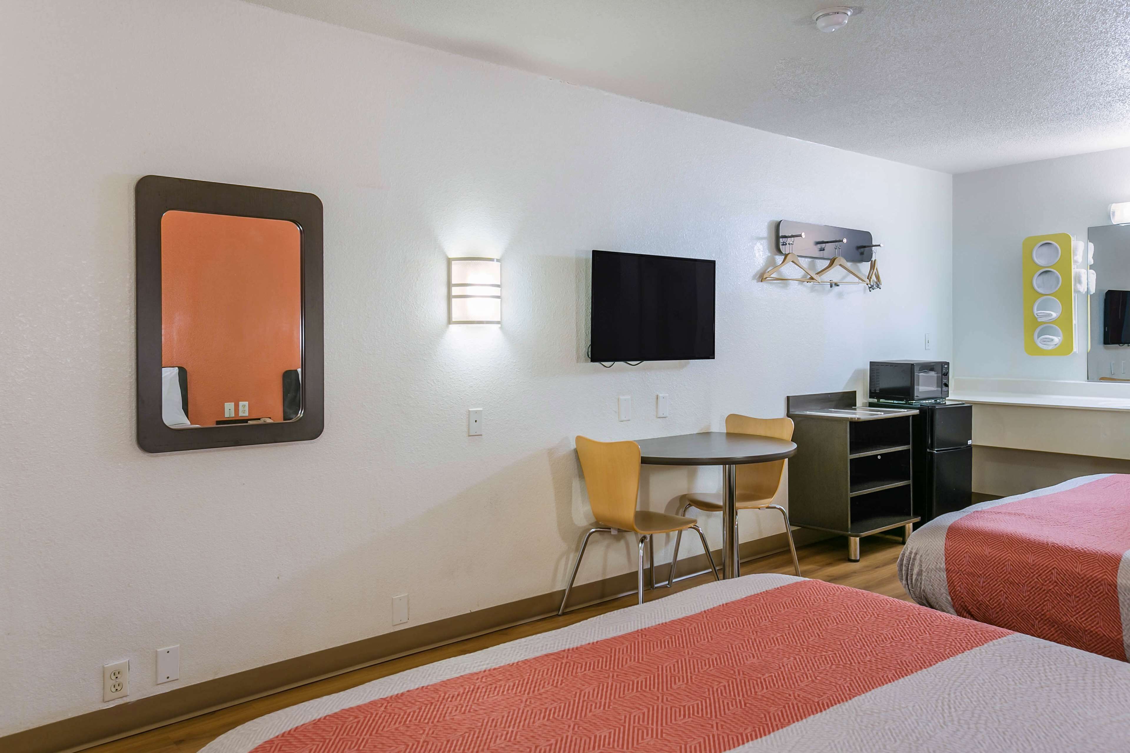 Una habitación de hotel con dos camas, un escritorio, una silla, un televisor y un espejo.