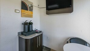 Una habitación con una televisión en la pared, una cafetera y un armario.