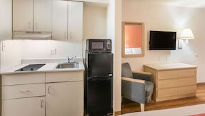 Una cocina compacta equipada con microondas, refrigerador y un pequeño comedor con una silla y una mesa.