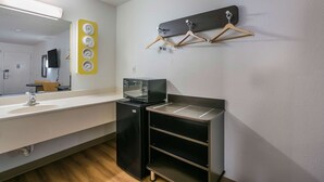 Habitación de hotel compacta con kitchenette, un espejo grande, un refrigerador negro, un microondas y un perchero de madera.