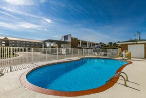 Una piscina con valla blanca, zona de estar techada y un edificio con un letrero que dice '6' al fondo.