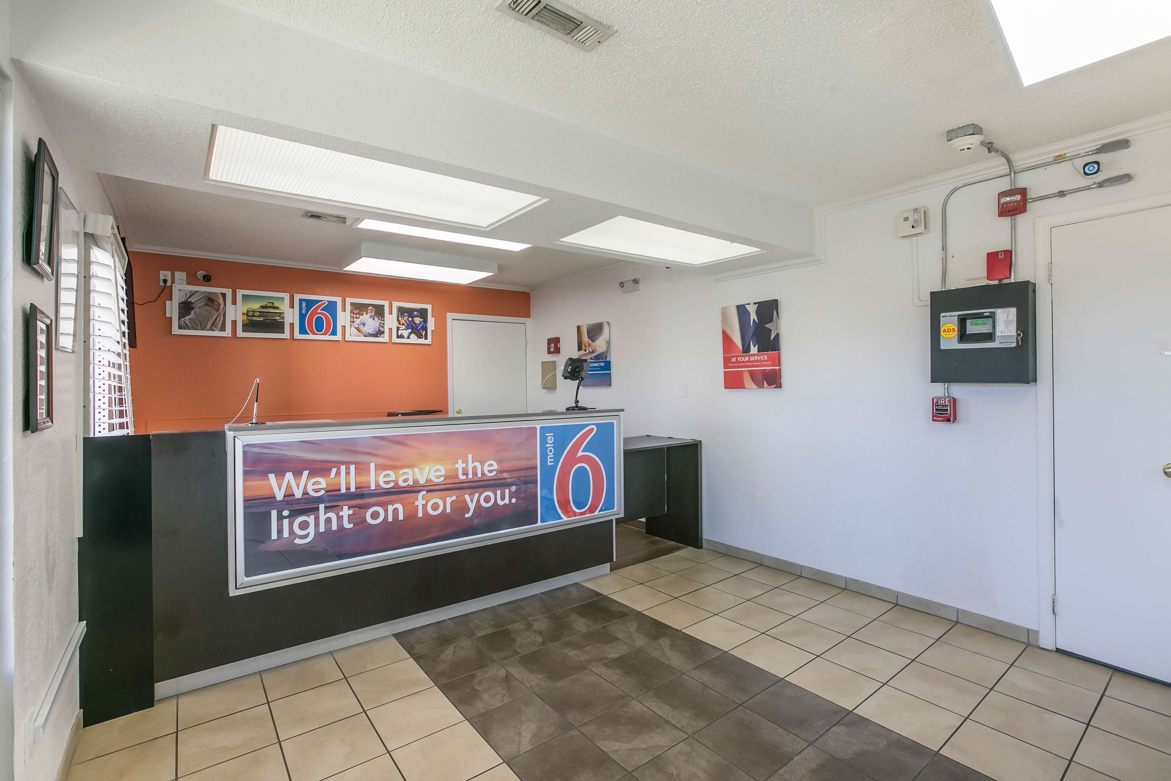 A hotel reception area with a counter, a fire alarm, and a sign indicating the hotel name.