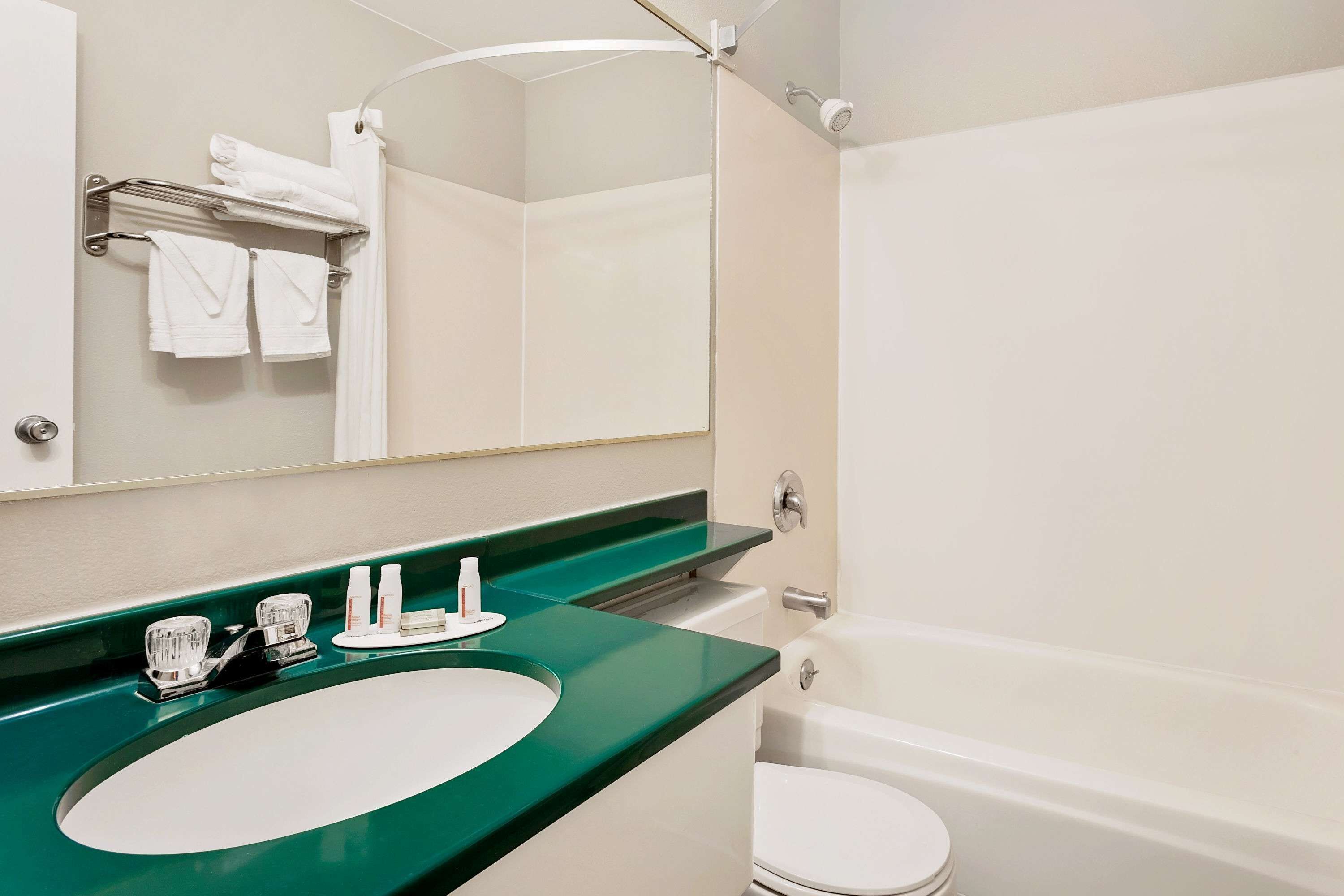 A bathroom with a green countertop sink, a white toilet, and a large mirror.