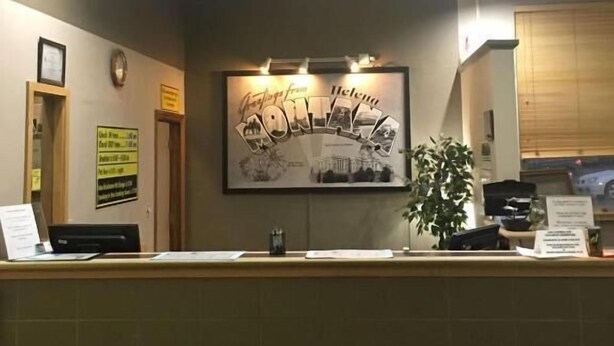 A reception desk with a framed welcome sign, a clock, and a potted plant. - Super 8 by Wyndham Helena (Helena)