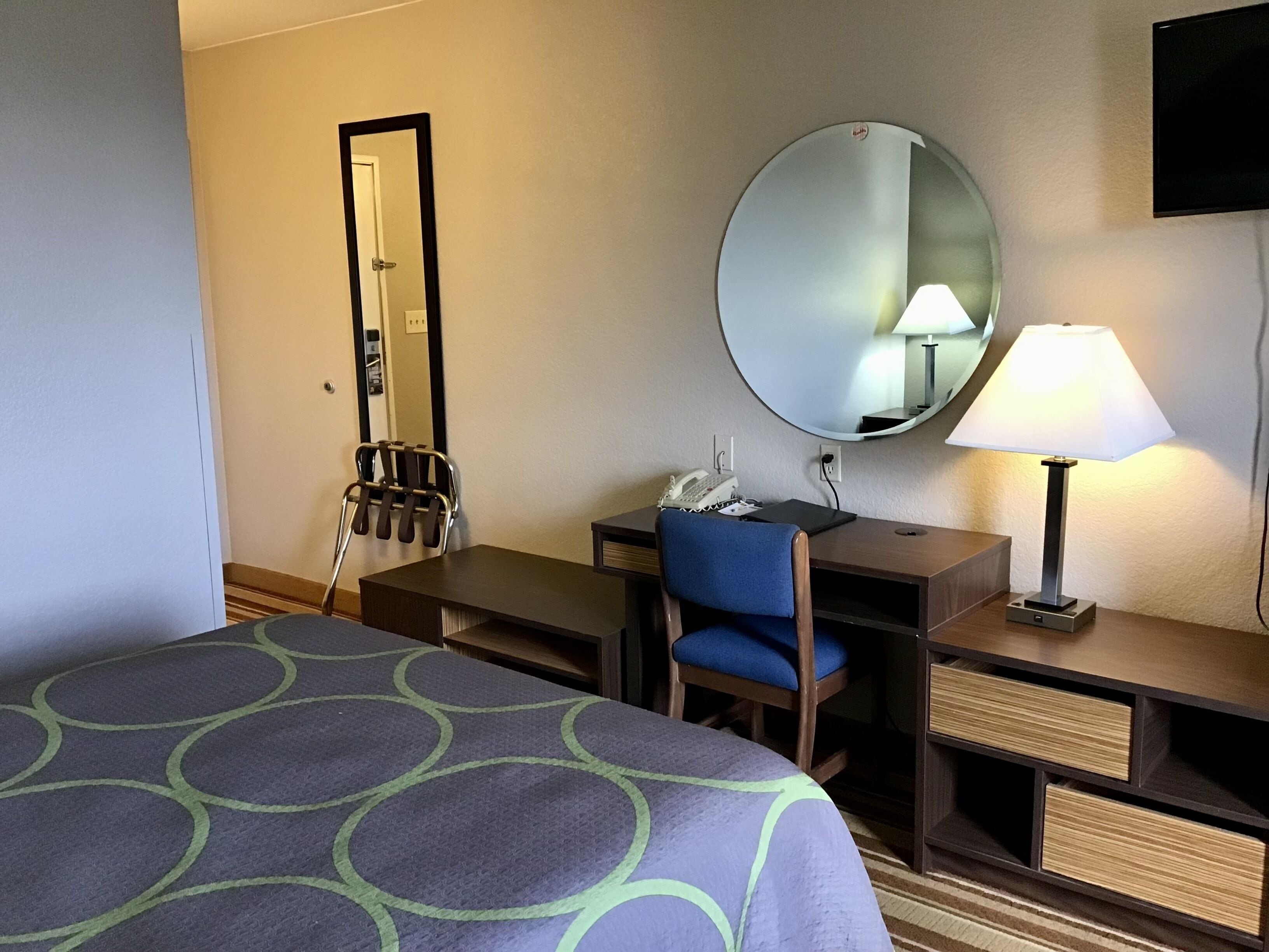 Ein Hotelzimmer mit Bett, Schreibtisch, Stuhl, Spiegel, Lampe und Telefon.