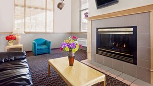 A room with a fireplace, a blue armchair, a black leather sofa, and a vase with flowers. - Super 8 by Wyndham Helena (Helena)
