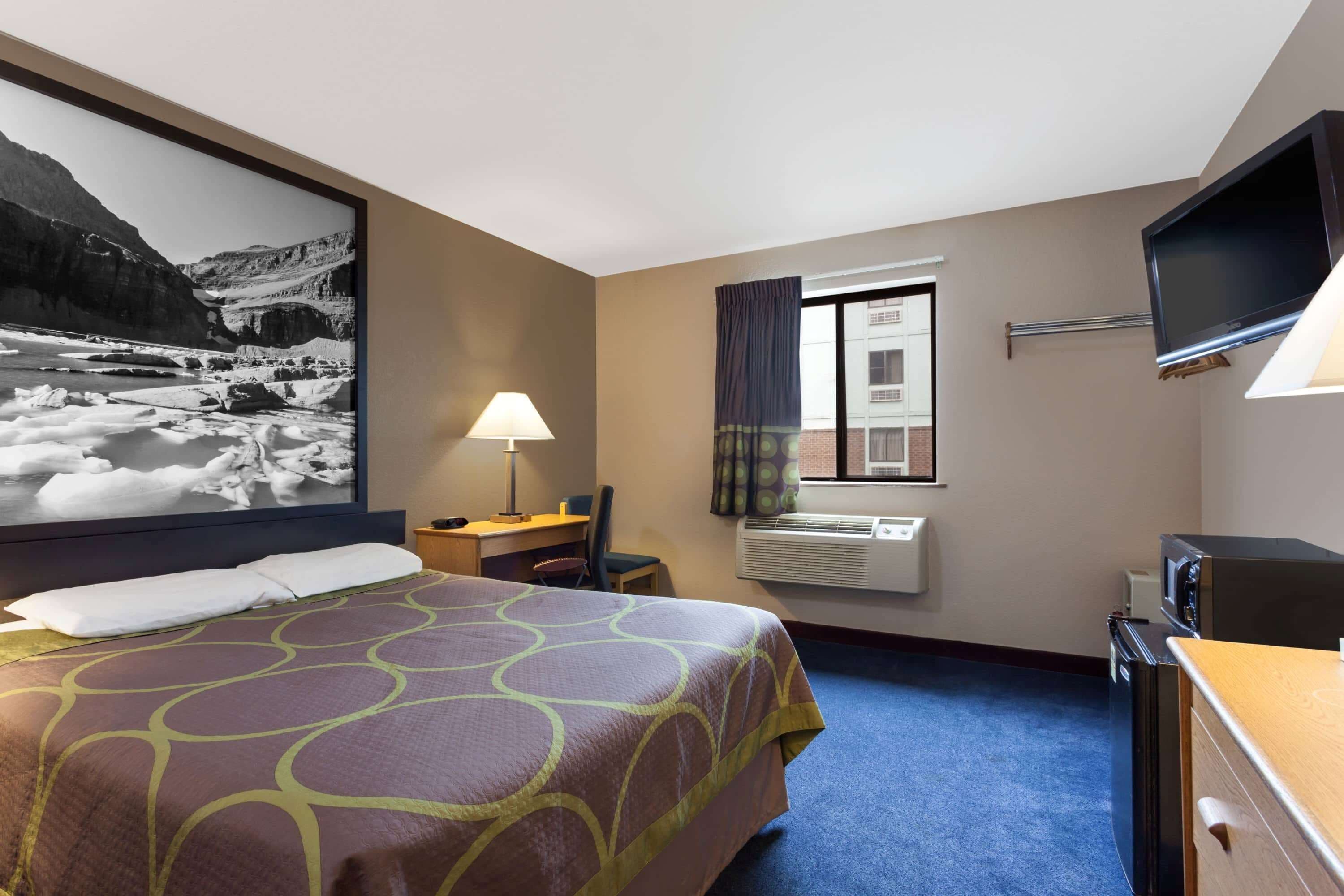 A hotel room with a large bed, a desk, a chair, a TV, and a window with curtains.