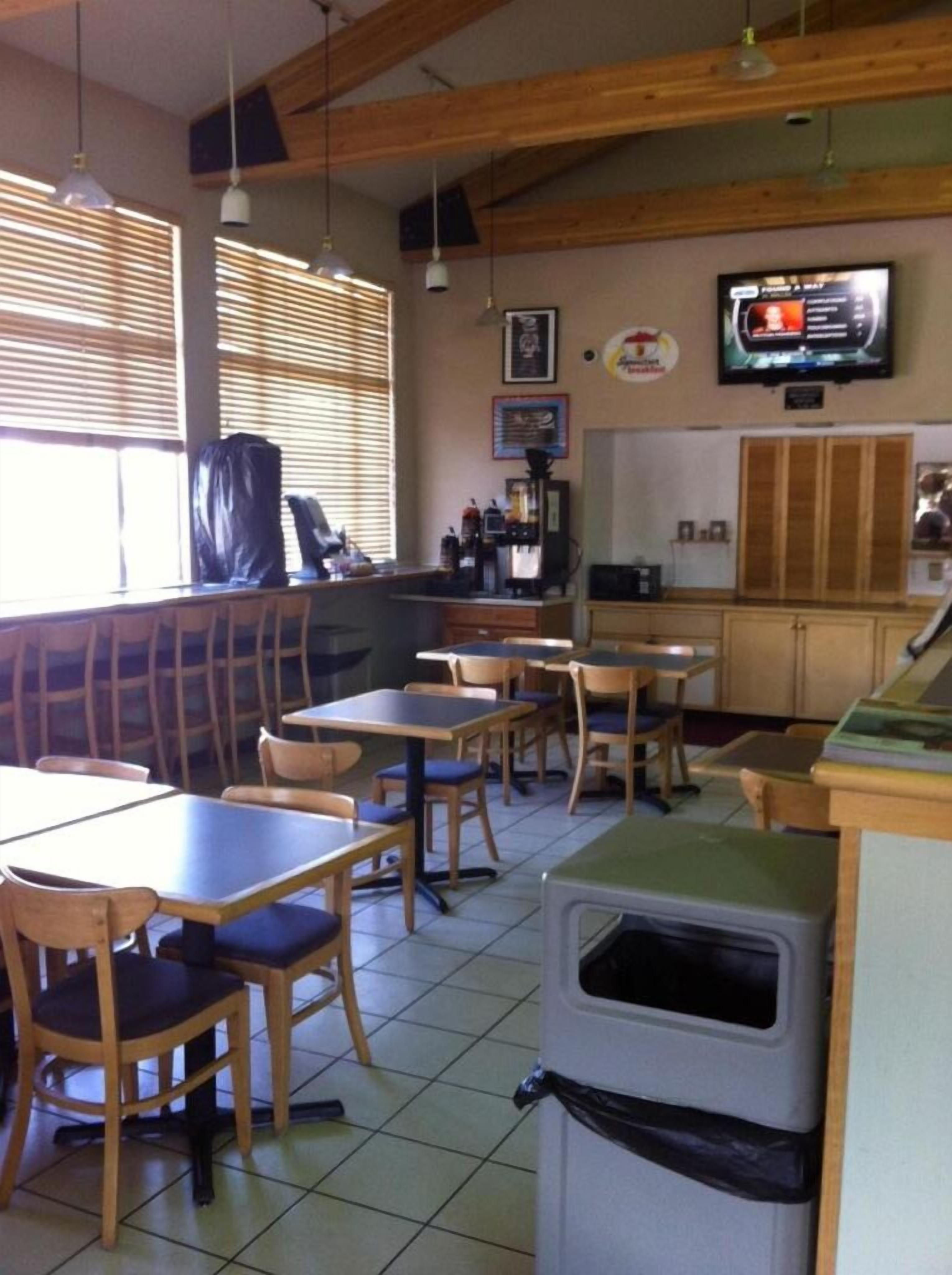 A restaurant interior with wooden tables and chairs, a television on the wall, and a trash bin.