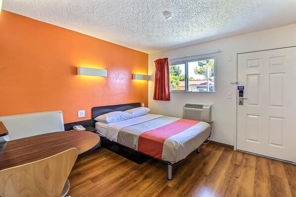 Habitación de hotel con cama, escritorio, silla, ventana con cortinas y puerta.