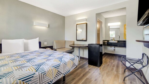 A hotel room with a bed, a desk, a chair, a small refrigerator, a sink, and a mirror. - Motel 6 San Jose, CA - Airport (San Jose)