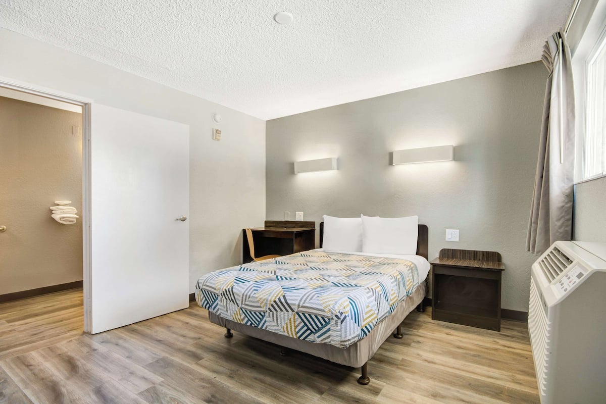 A hotel room with a bed, bedside tables, a heater, and a door.