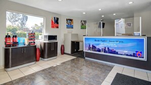 A modern reception area with a digital screen displaying a cityscape, a coffee station, and a view of the outdoors. - Motel 6 San Jose, CA - Airport (San Jose)