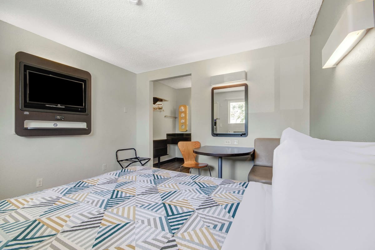 A hotel room with a bed, a desk, a chair, a TV, and a mirror.