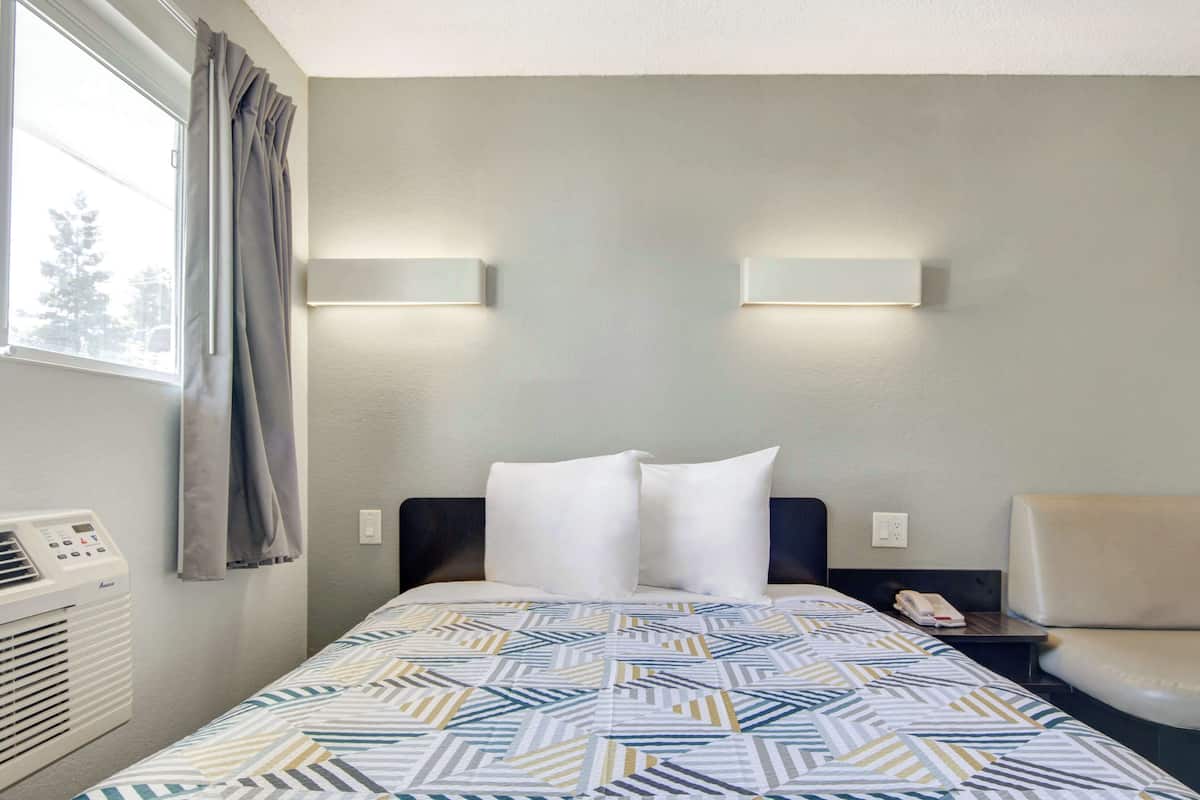 A hotel room with a bed, two bedside lamps, a chair, a heater, and a window with curtains.