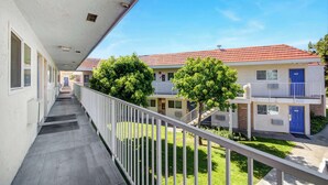A corridor with a white railing, leading to a building with a red-tiled roof and a blue door. - Motel 6 San Jose, CA - Airport (San Jose)