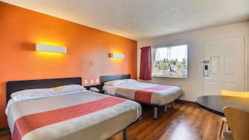 Habitación de hotel con dos camas, piso de madera, ventana con vistas y una mesa con sillas.