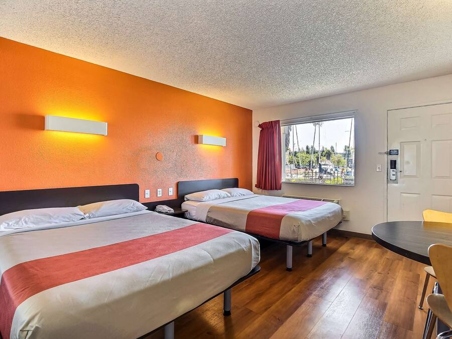 Habitación de hotel con dos camas, piso de madera, ventana con vistas y una mesa con sillas.