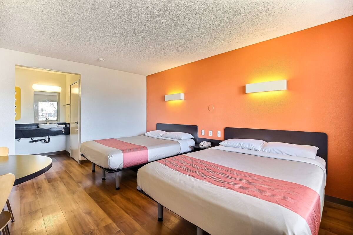 A hotel room with two beds, a small desk, and a bathroom visible through an open door.