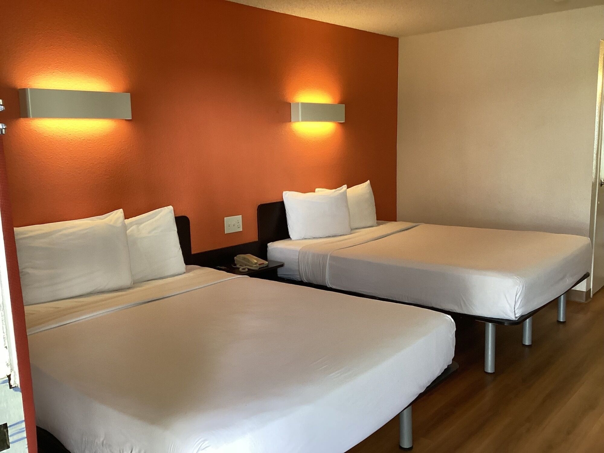 Une chambre d’hôtel avec deux lits simples, une table de chevet avec un téléphone et des lampes fixées au mur.