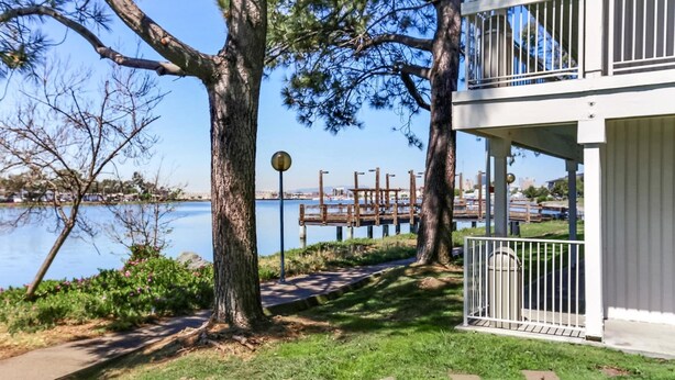 A lakeside property with a wooden dock, a covered outdoor seating area, and a pathway leading to the water. - Motel 6 Oakland, CA - Embarcadero (Oakland)