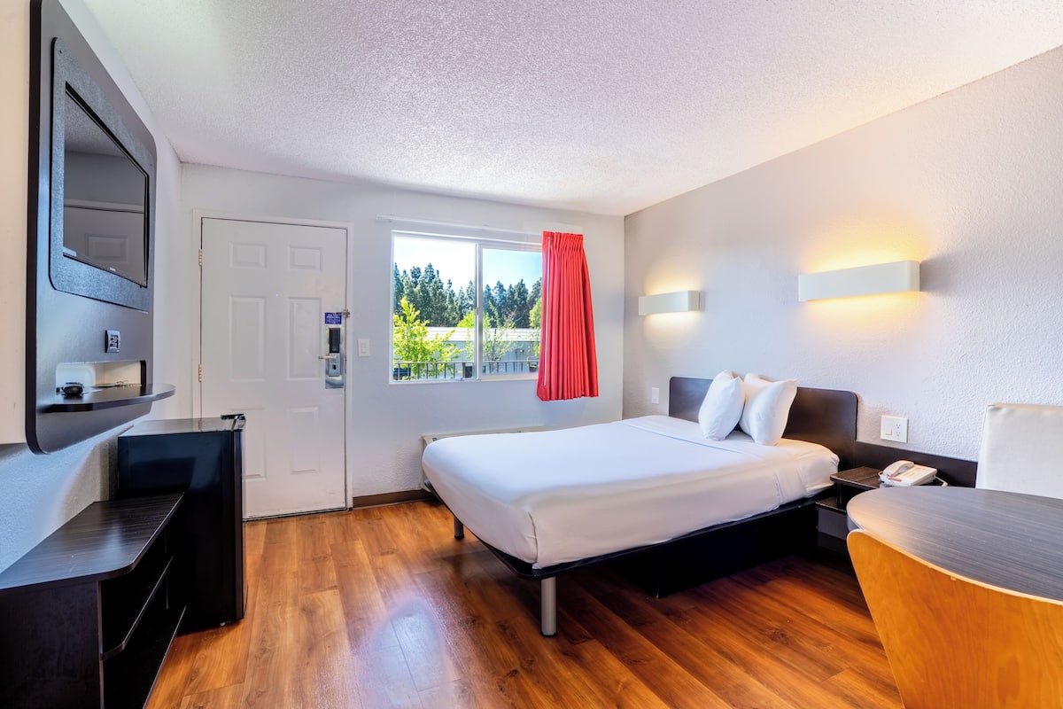 Habitación de hotel con cama, mesita de noche, escritorio, silla, ventana con vistas y puerta.