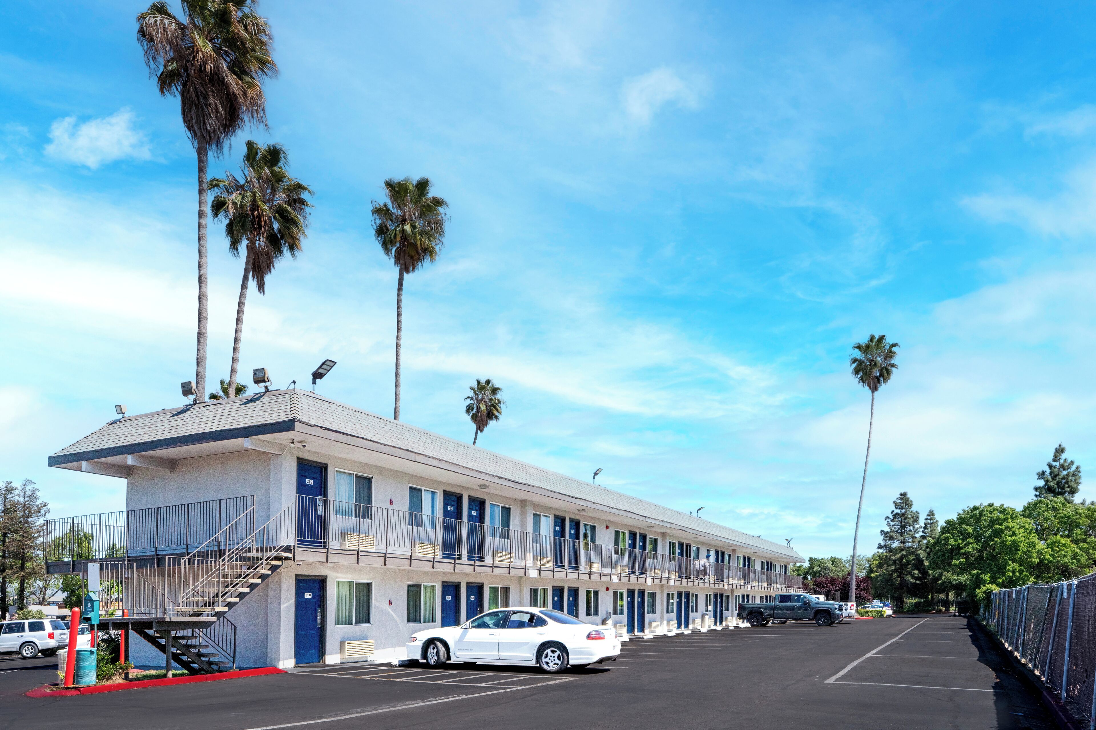 A motel with a two-story structure, a parking lot, and palm trees.