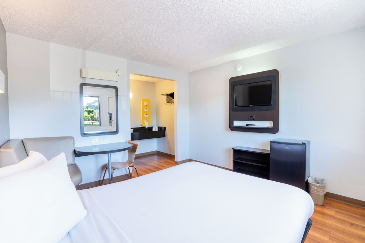 Habitación de hotel con cama, escritorio, silla, televisor y refrigerador pequeño.