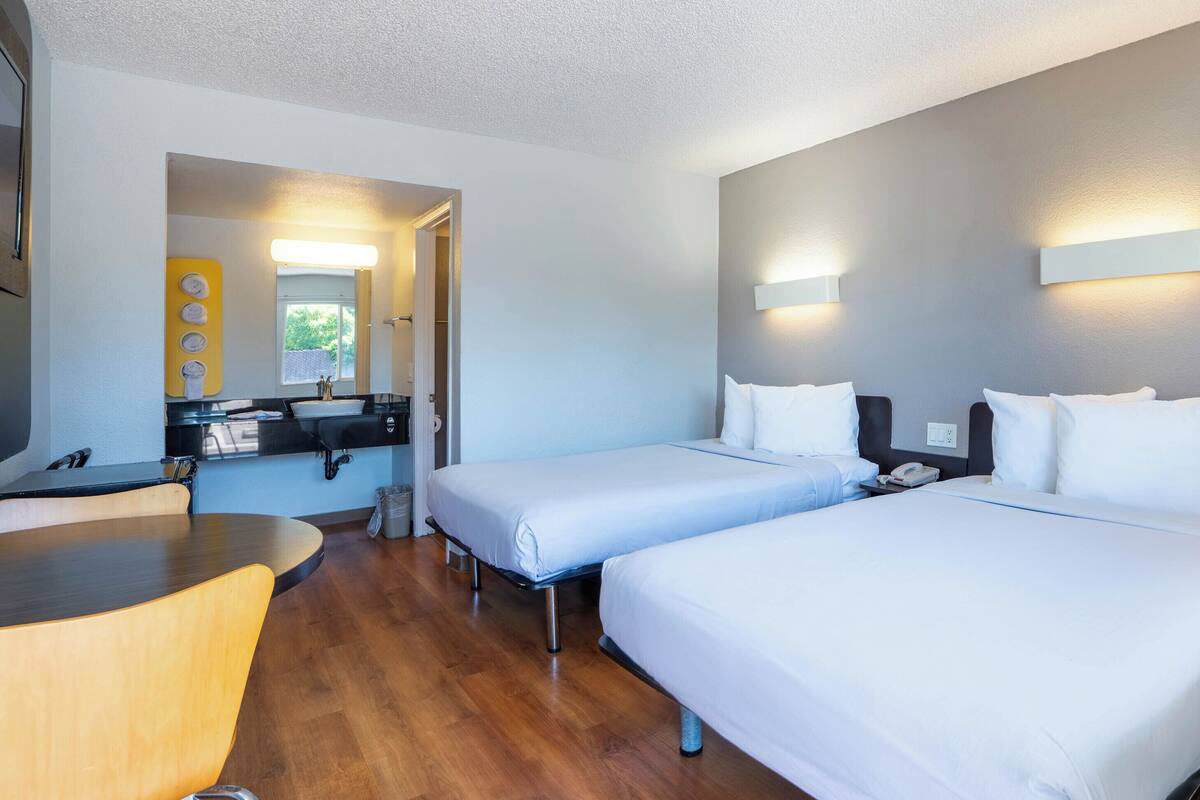 Habitación de hotel con dos camas, un escritorio, un lavamanos y un espejo.