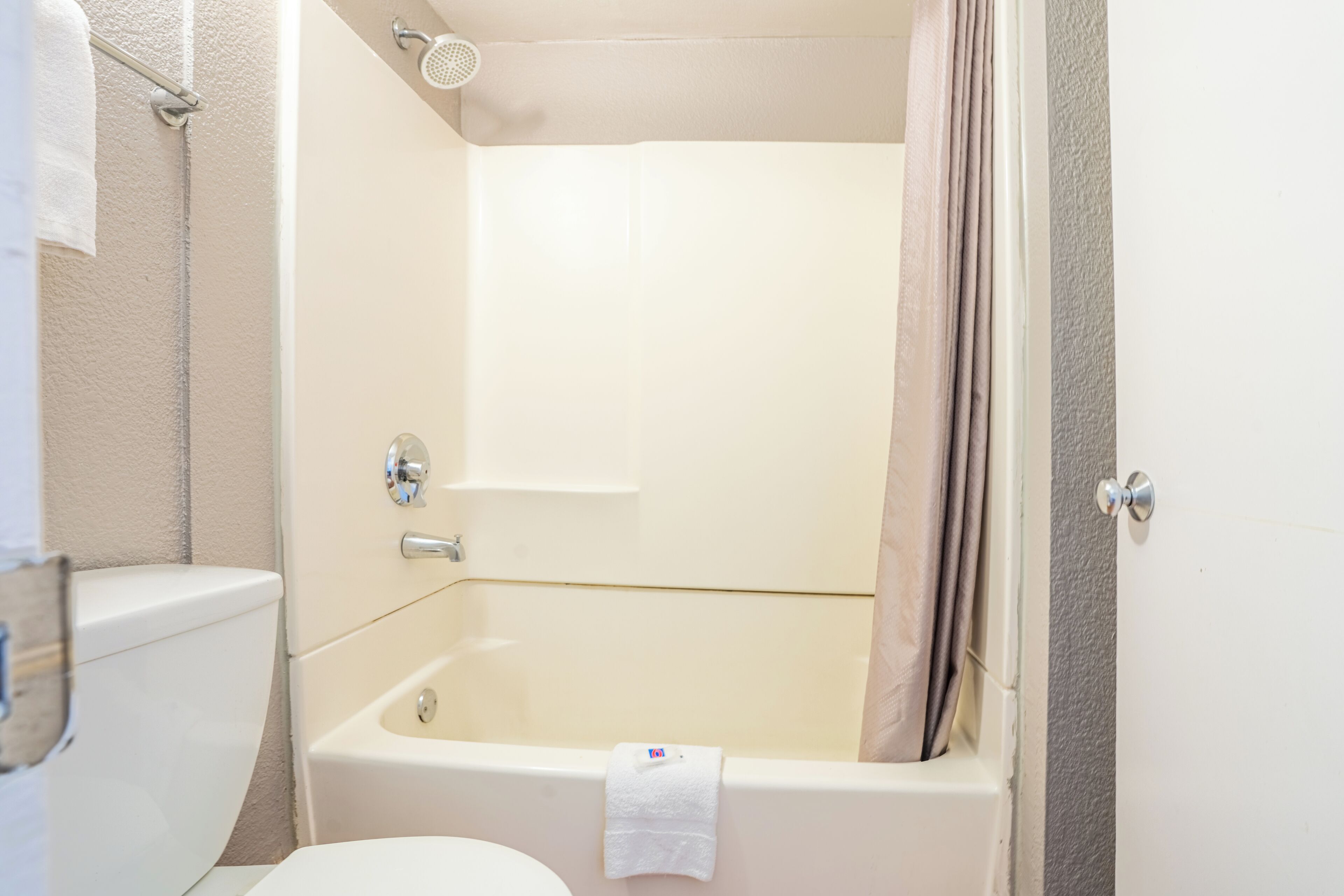 A bathroom with a toilet, bathtub, shower, and a towel hanging on the wall.