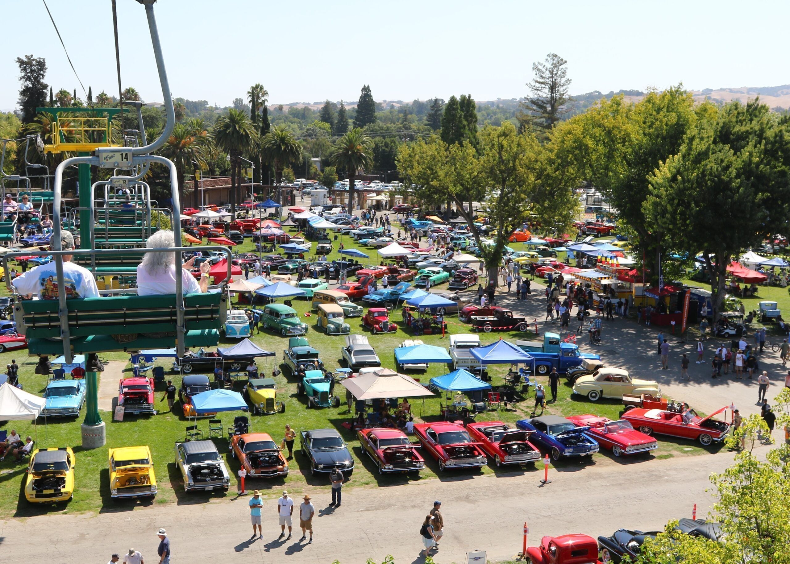 A parking lot with various vintage cars and a green chairlift.