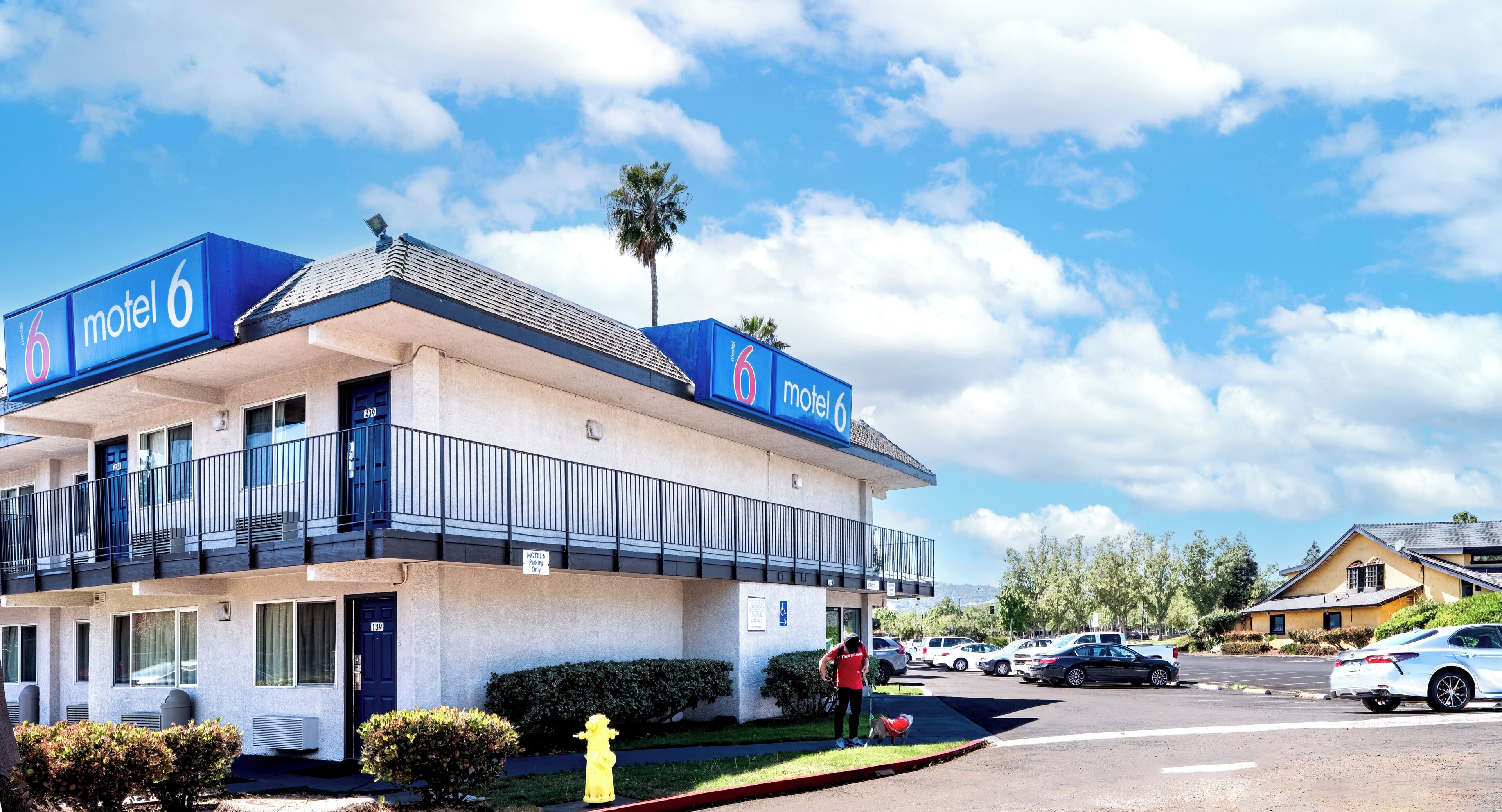 A motel with a two-story structure, a parking lot, and a clear sky.