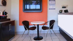 A small, modern kitchen area with a round table and two chairs, a built-in oven, and a digital screen mounted on the wall. - Super 8 by Wyndham Walnut Creek (Walnut Creek)