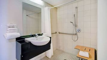 A bathroom with a sink, mirror, shower, and a small wooden table.