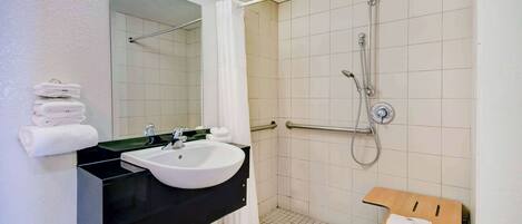 A bathroom with a sink, mirror, shower, and a small wooden table.