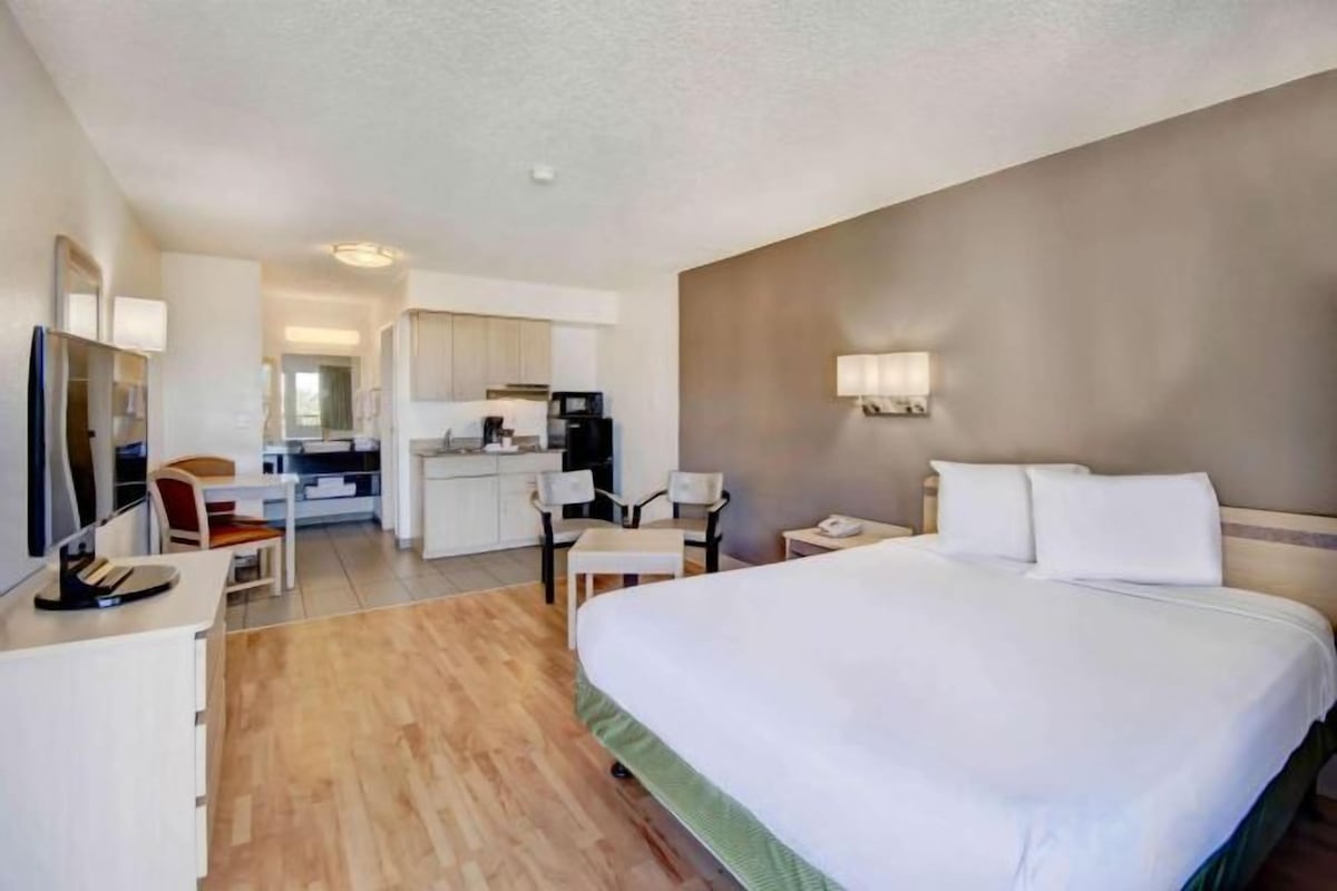 Habitación de hotel con una cama grande, un escritorio, una silla, un televisor y una kitchenette.