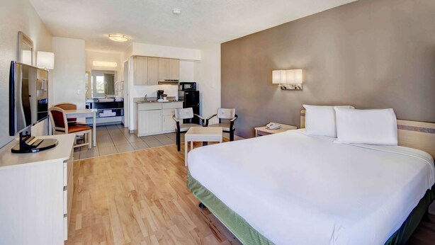 A hotel room with a large bed, a desk with a chair, a kitchenette, and a bathroom.