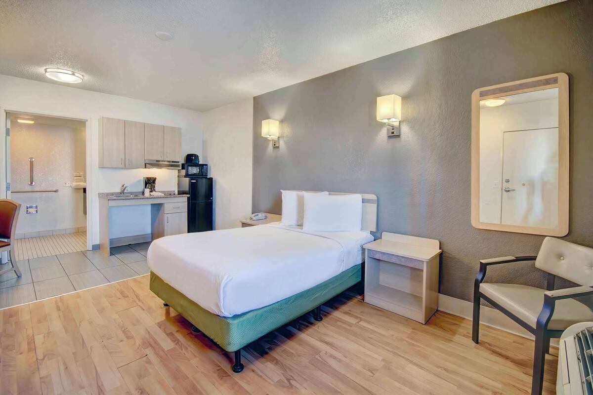 Una camera d'albergo con un letto, comodini, una poltrona, una scrivania con sedia e angolo cottura.