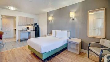 A hotel room with a bed, bedside tables, a chair, a desk with a chair, and a kitchenette.