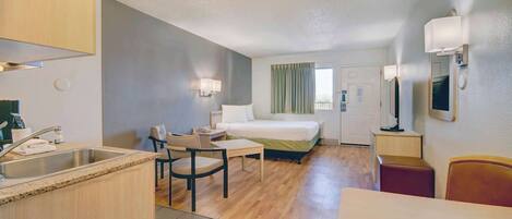 Una habitación de hotel compacta con kitchenette, una cama, un escritorio y una silla.
