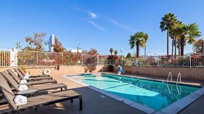 Un espace piscine avec des chaises longues, un poste de surveillance pour les sauveteurs et une clôture blanche ornée de fleurs.