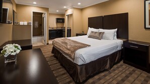 A hotel room with a large bed, a desk, a chair, a small table with a vase of flowers, a microwave, a sink, and a shower area. - Best Western Poway/San Diego Hotel (Poway)