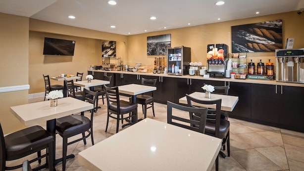 A restaurant with multiple tables and chairs, a counter with a coffee machine, and a television mounted on the wall. - Best Western Poway/San Diego Hotel (Poway)