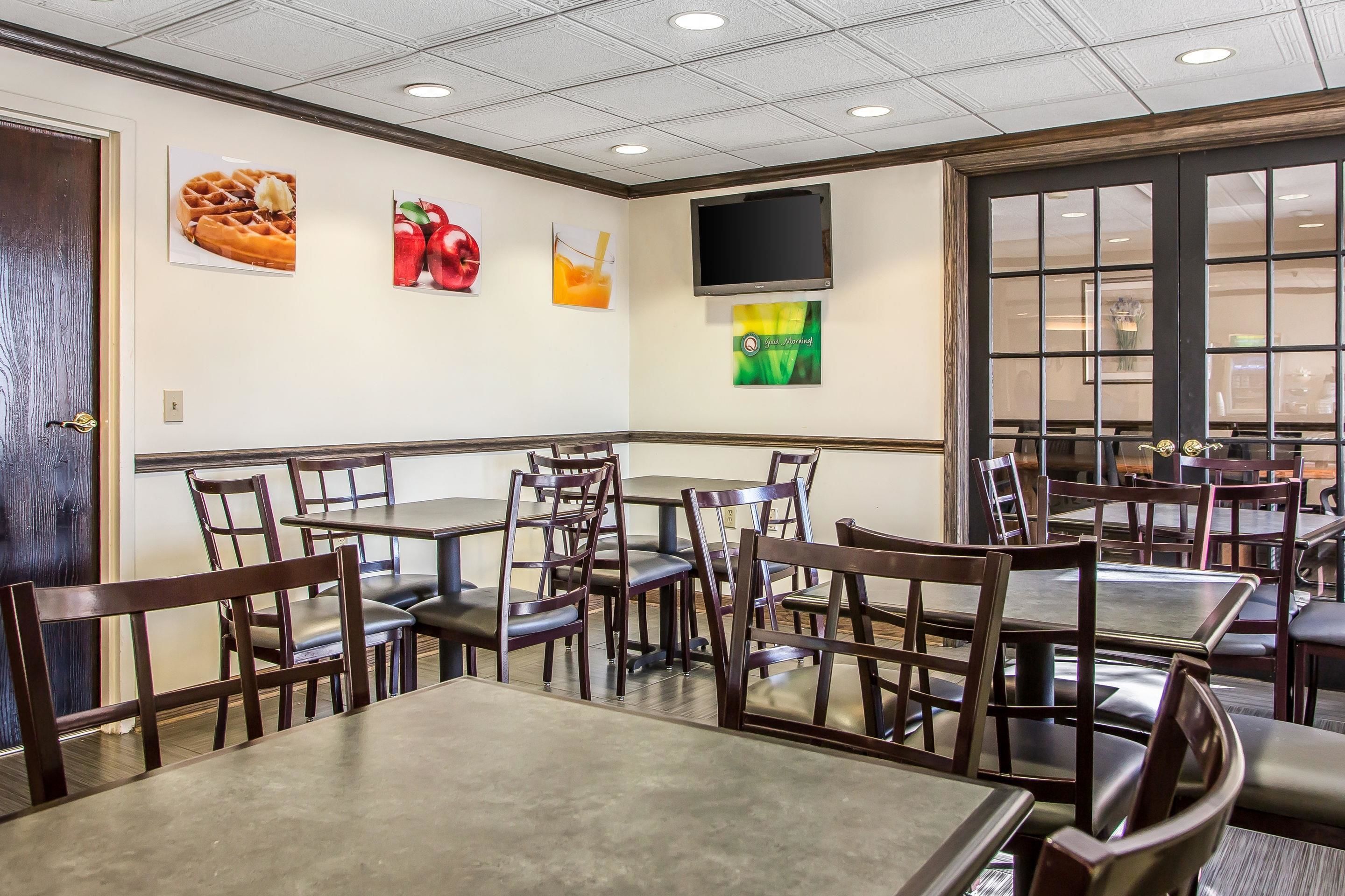Interior de un restaurante con mesas y sillas, un televisor montado en la pared y decoración que muestra comida y bebidas.