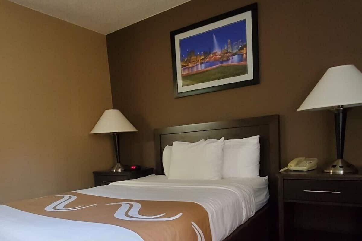 A hotel room with a large bed, two bedside tables with lamps, a framed picture on the wall, and a carpeted floor.