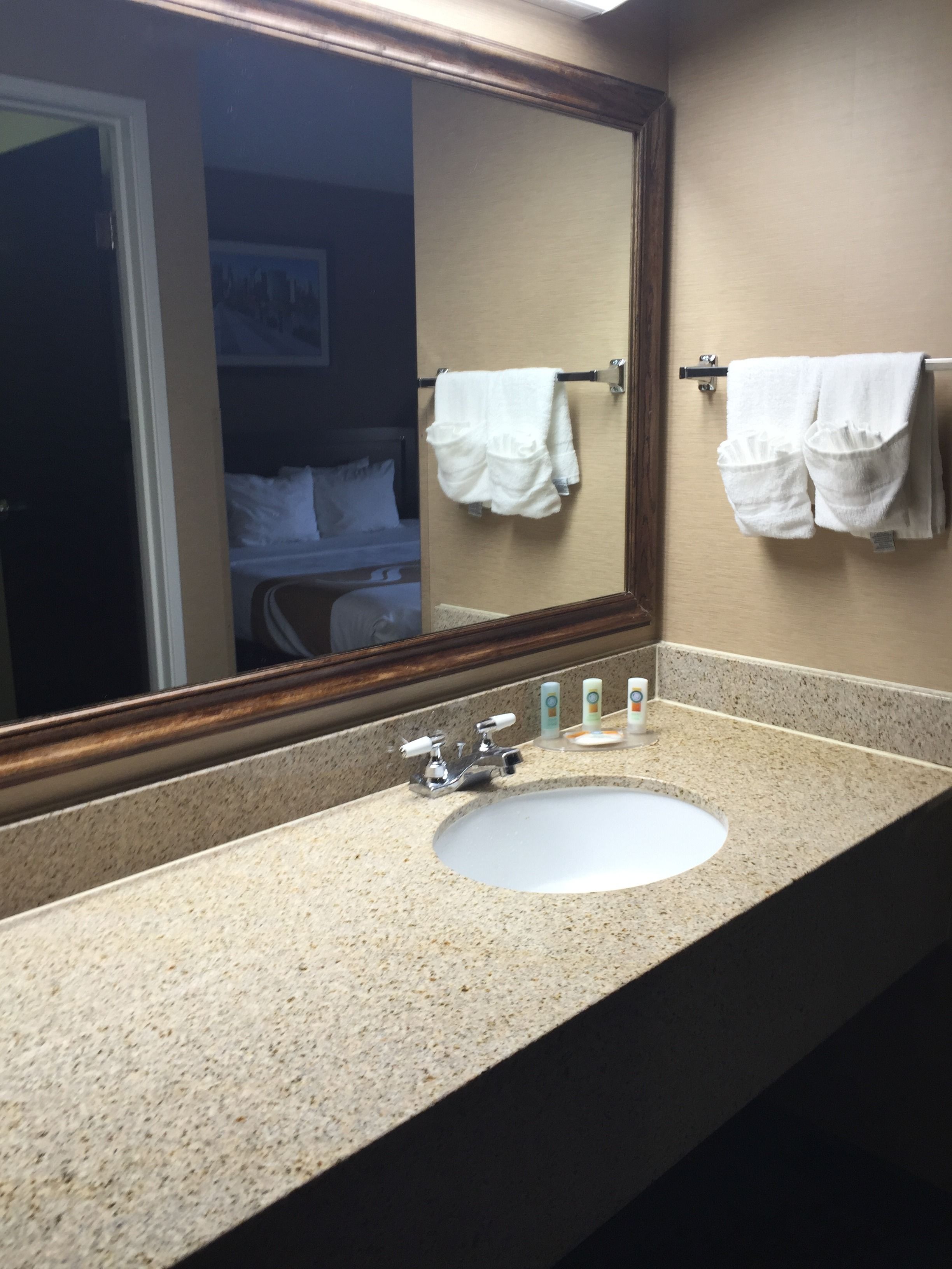 A bathroom with a granite countertop, a white sink, and a mirror. There are two white towels hanging on hooks.