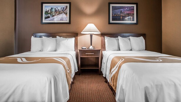 Habitación de hotel con dos camas, una mesita de noche con lámpara y dos cuadros en las paredes.