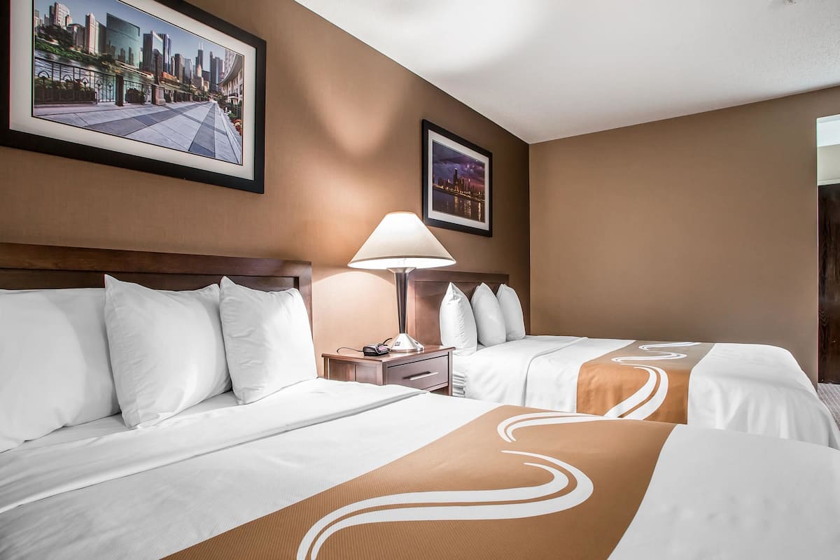 A hotel room with two beds, a nightstand, a lamp, and framed pictures on the wall.