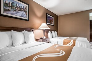 A hotel room with two beds, a nightstand, a lamp, and framed pictures on the wall.
