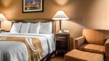 A hotel room with a bed, two bedside lamps, a nightstand, a chair, and a framed picture on the wall.